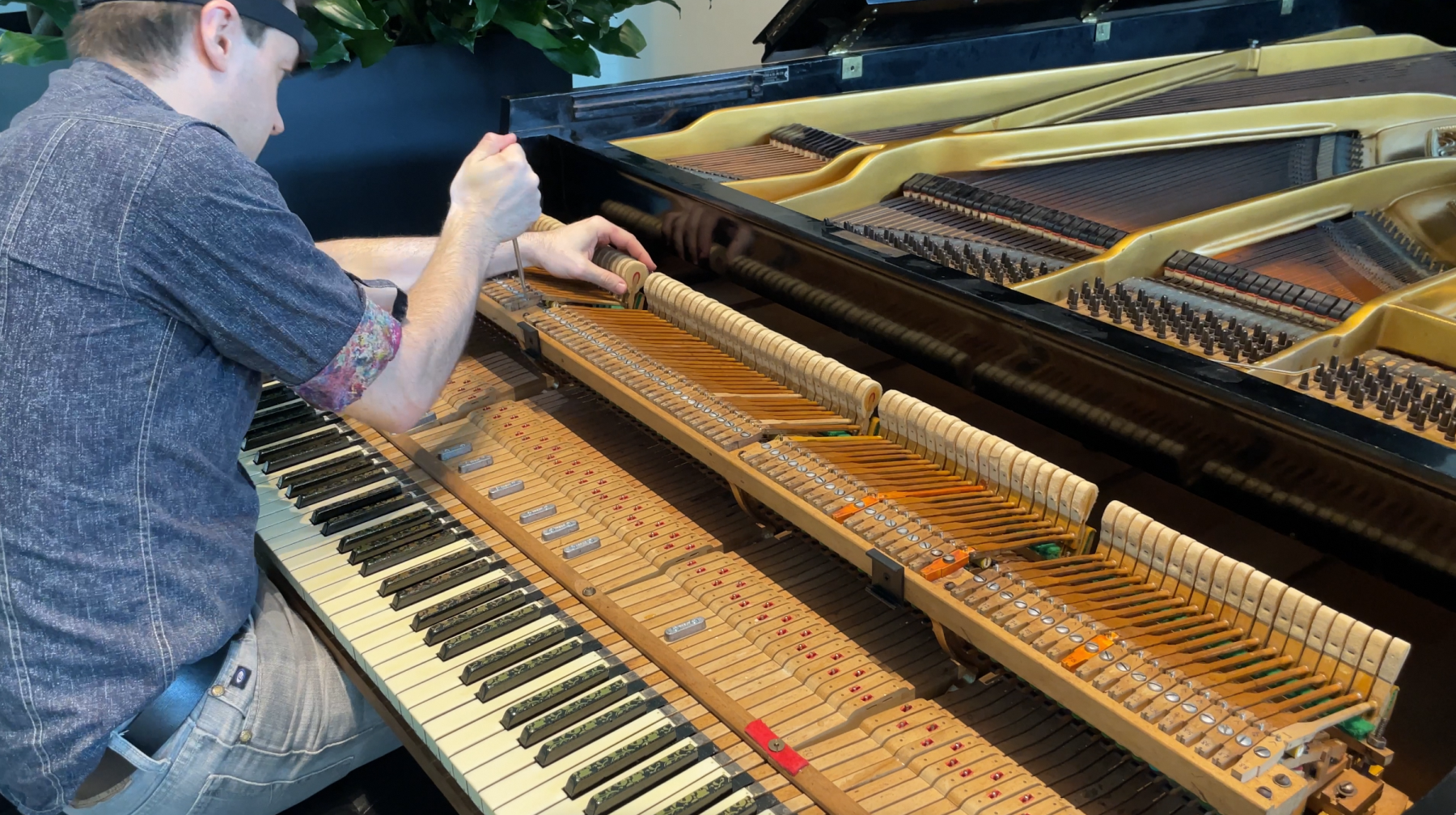 A person is repairing an open grand piano, adjusting the action components above the keyboard.